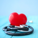 A red heart is sitting on top of a stethoscope on a blue wooden table.