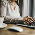 A woman is sitting at a table typing on a laptop computer.