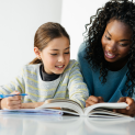 A woman is helping a young girl with her homework.