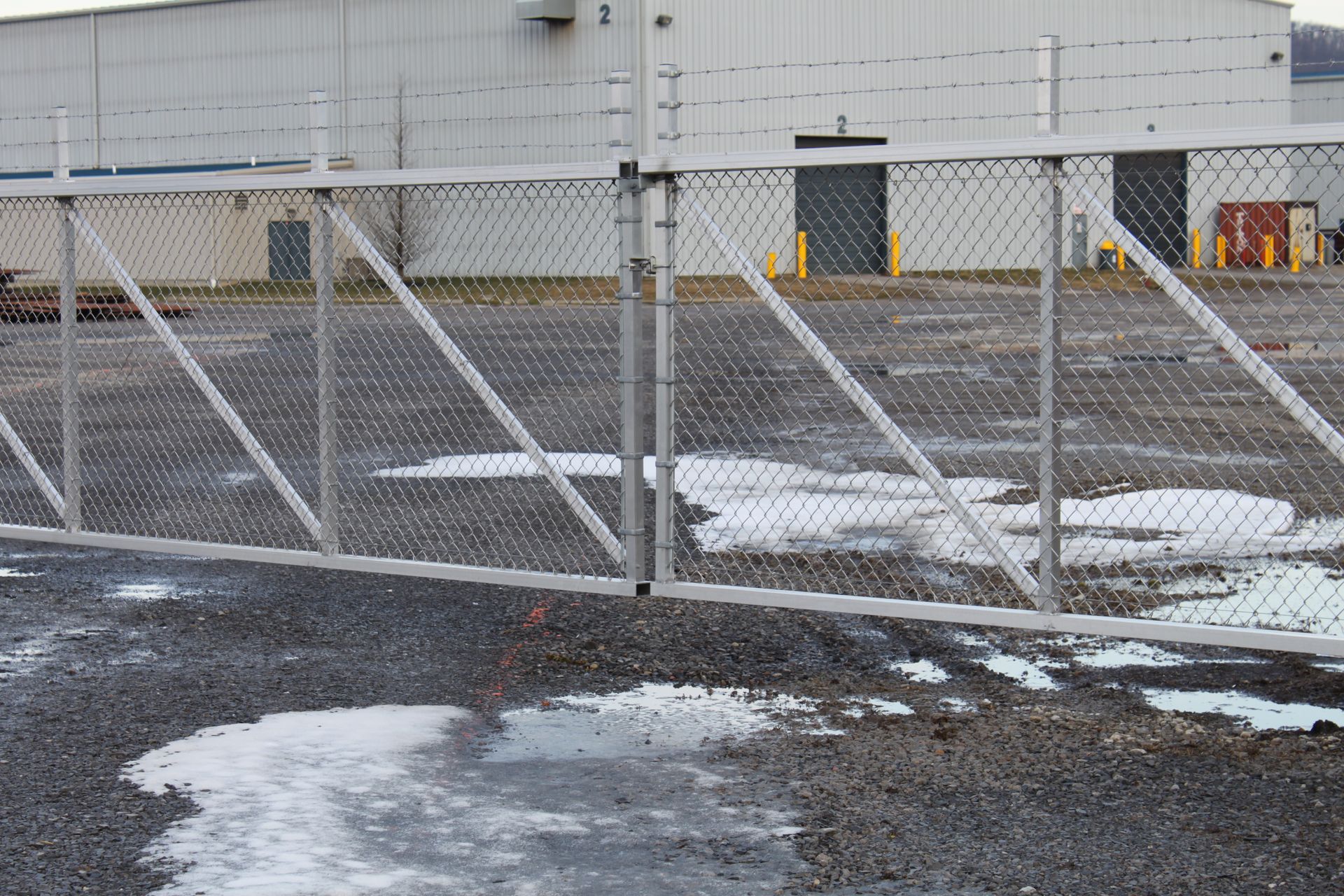 A chain link fence surrounds a parking lot with a building in the background.