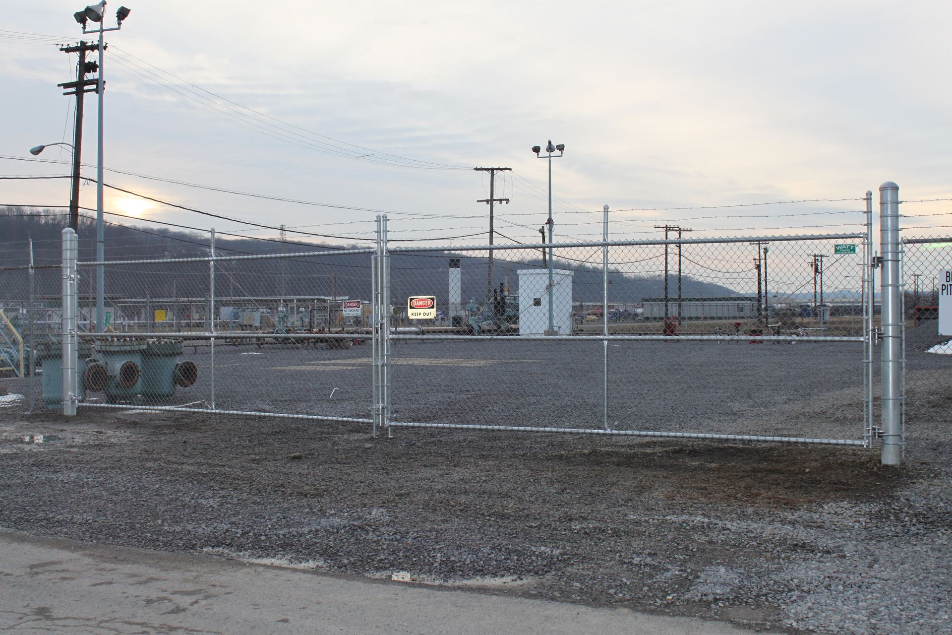 A chain link fence surrounds a gravel area with a transformer in the background