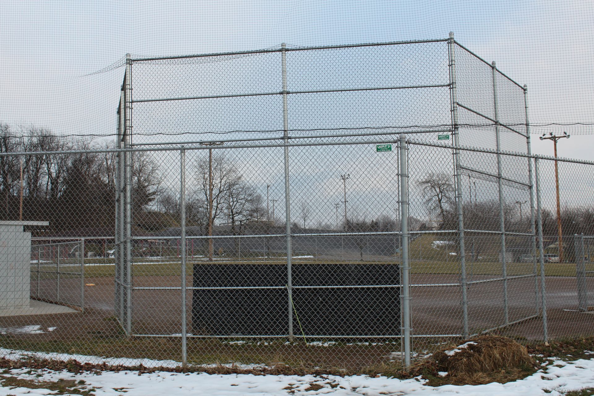A chain link fence surrounds a baseball field with snow on the ground