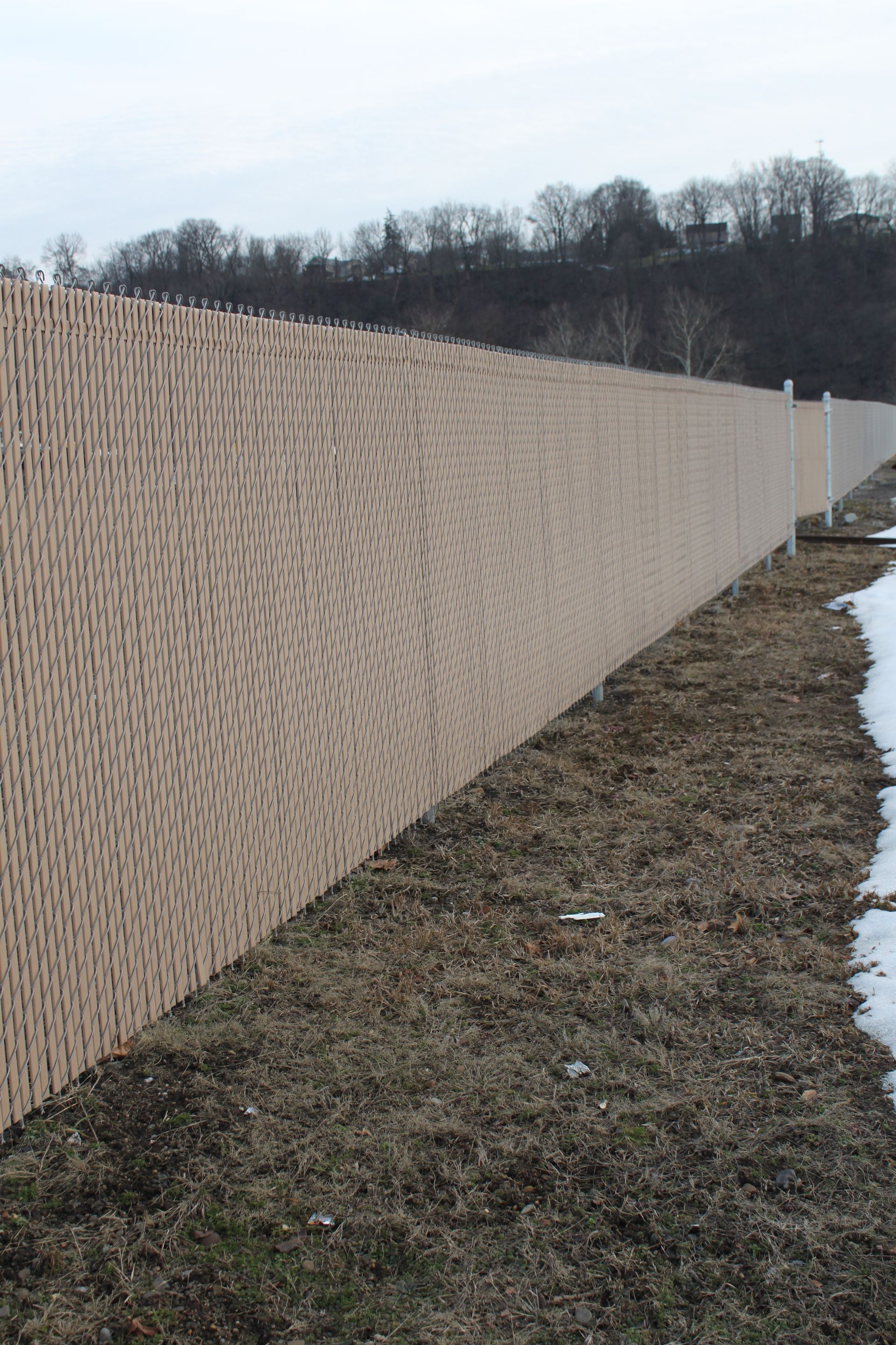 A long chain link fence surrounds a grassy field.