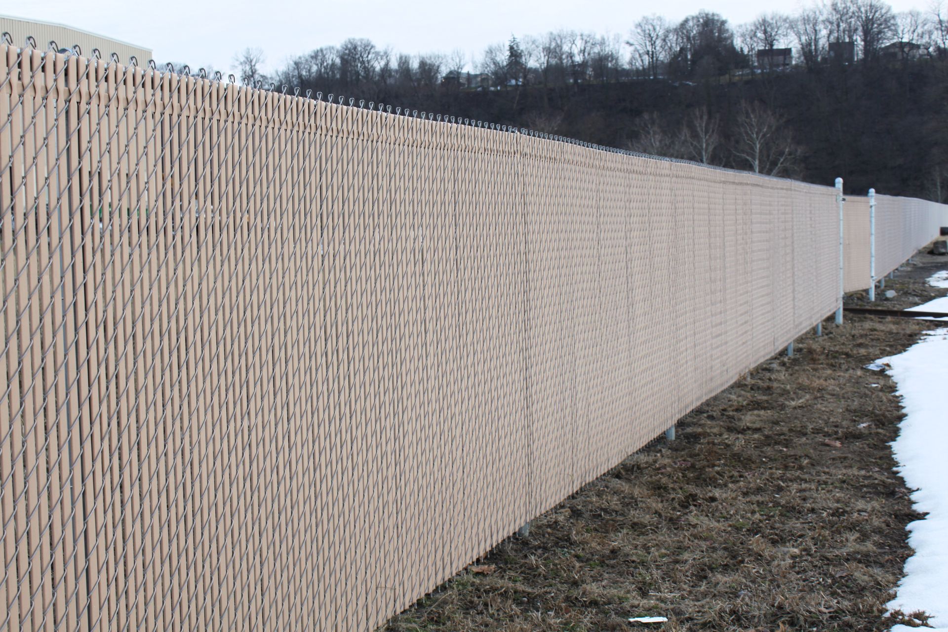 A long chain link fence surrounds a field with snow on the ground.