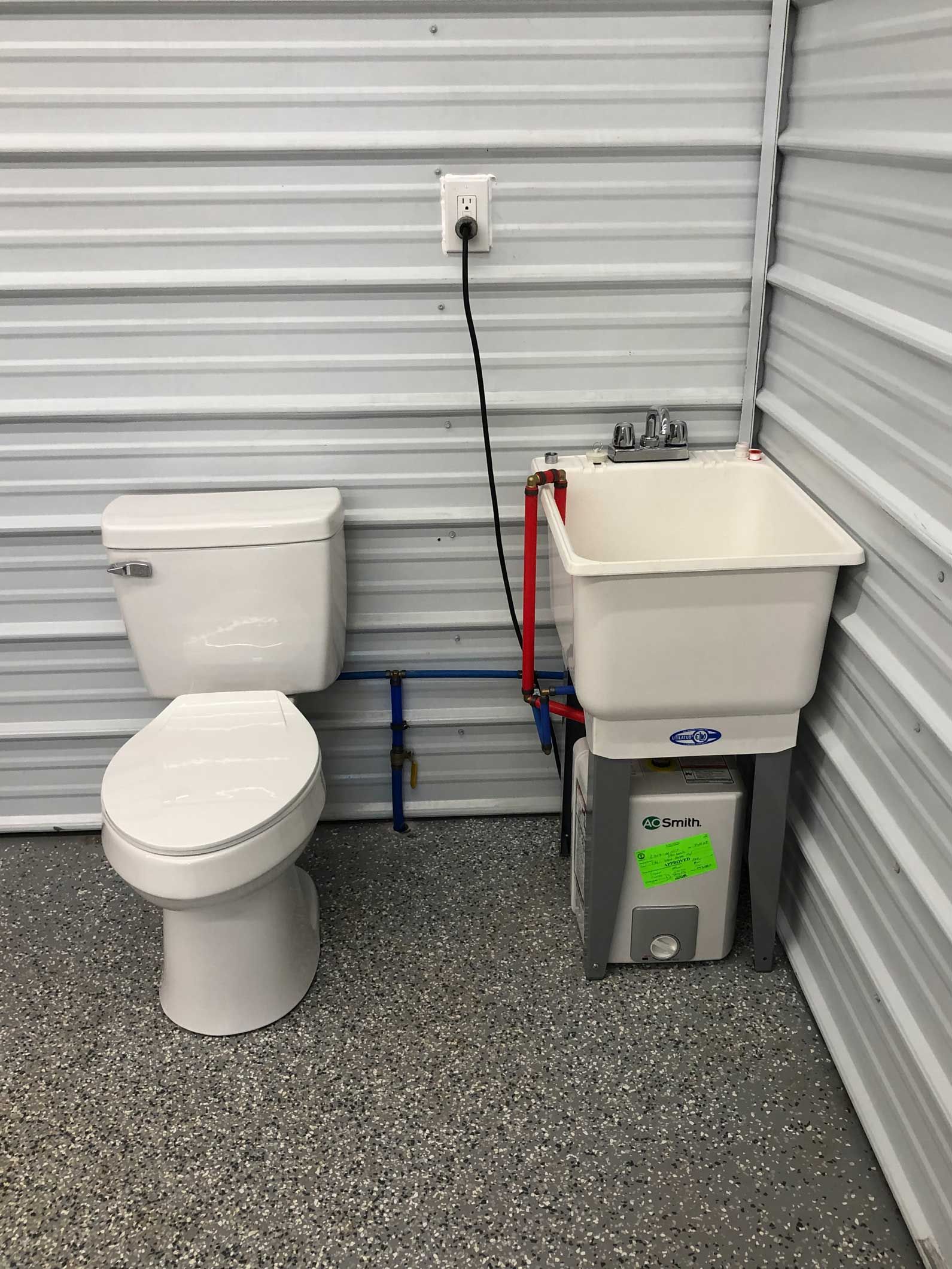 Toilet and utility sink in a room with metal walls and a gray floor.