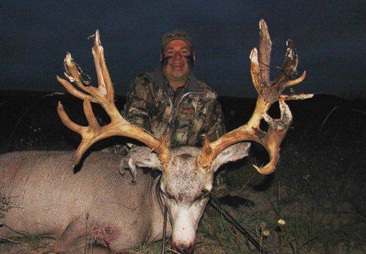 Hunter in camo with large buck. Buck's antlers are wide. Dark setting.