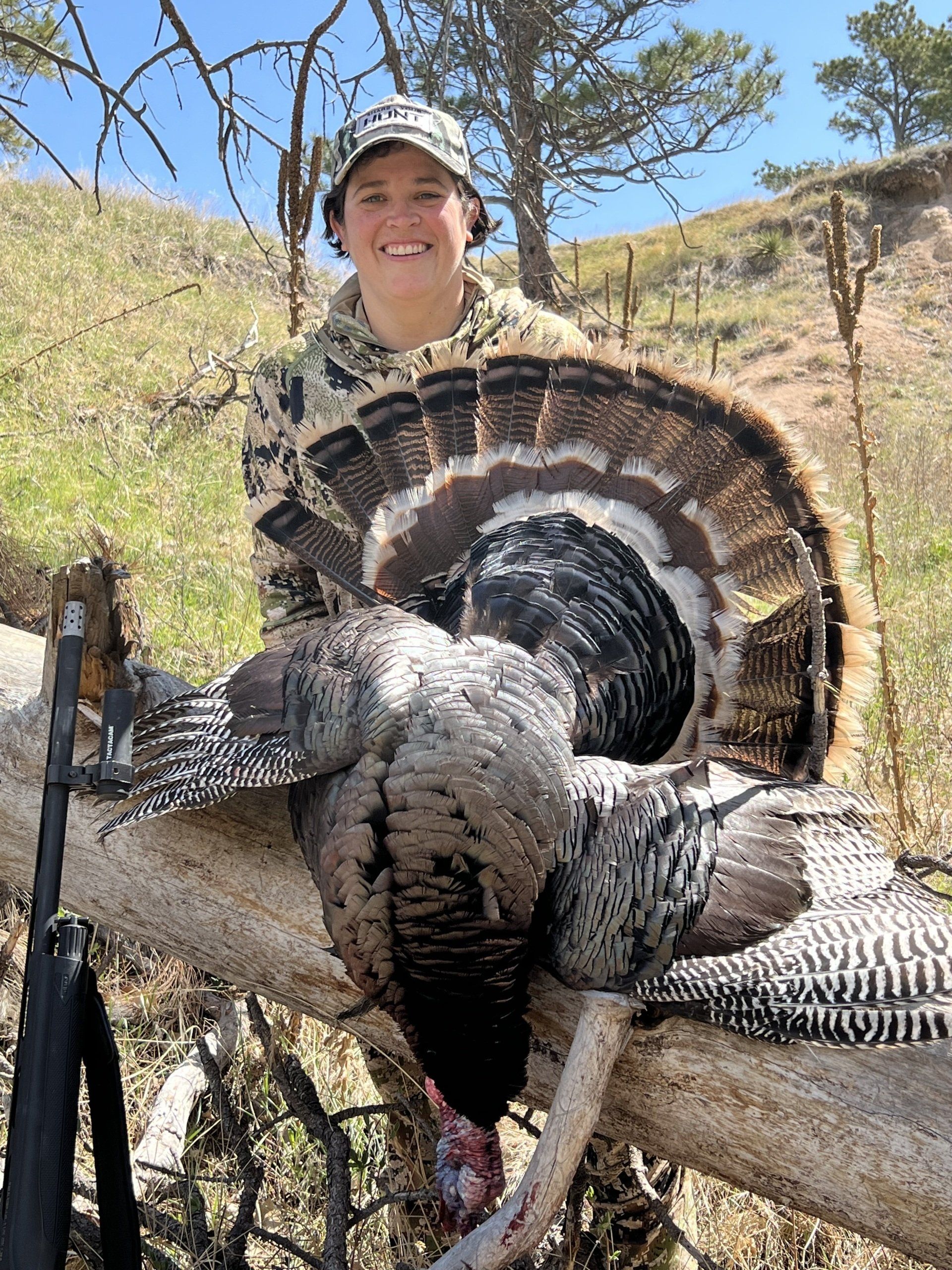 Hunter in camouflage smiling with a harvested turkey, outdoors.