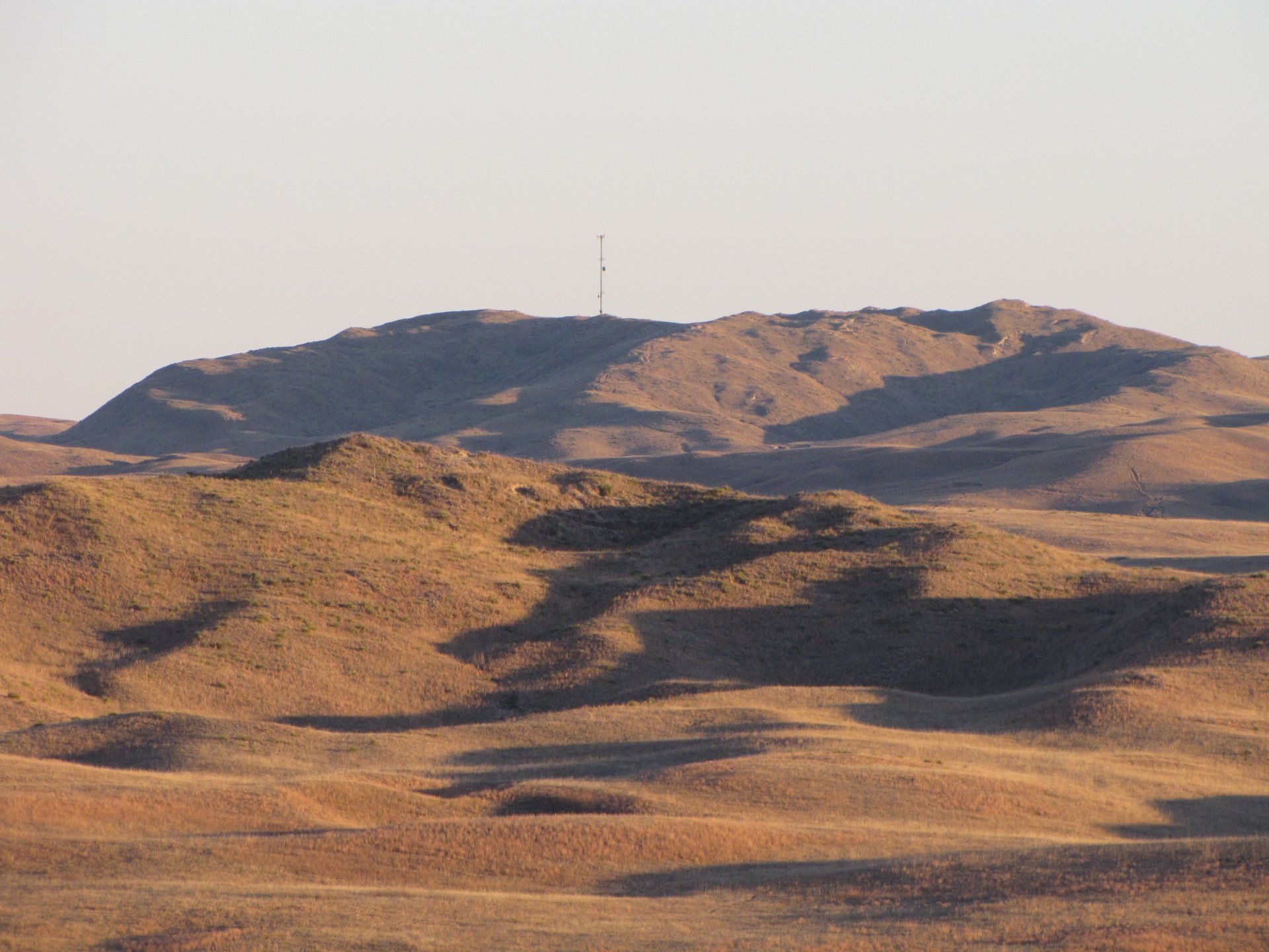 Hilly landscape in warm sunlight with a communications tower on the highest peak.