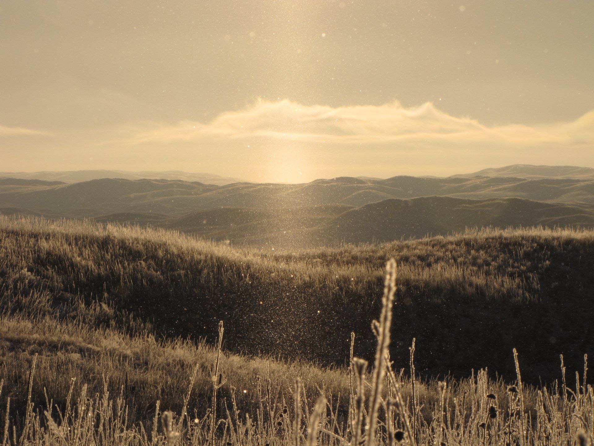Fields of frosted grass and rolling hills under a bright, hazy sky.