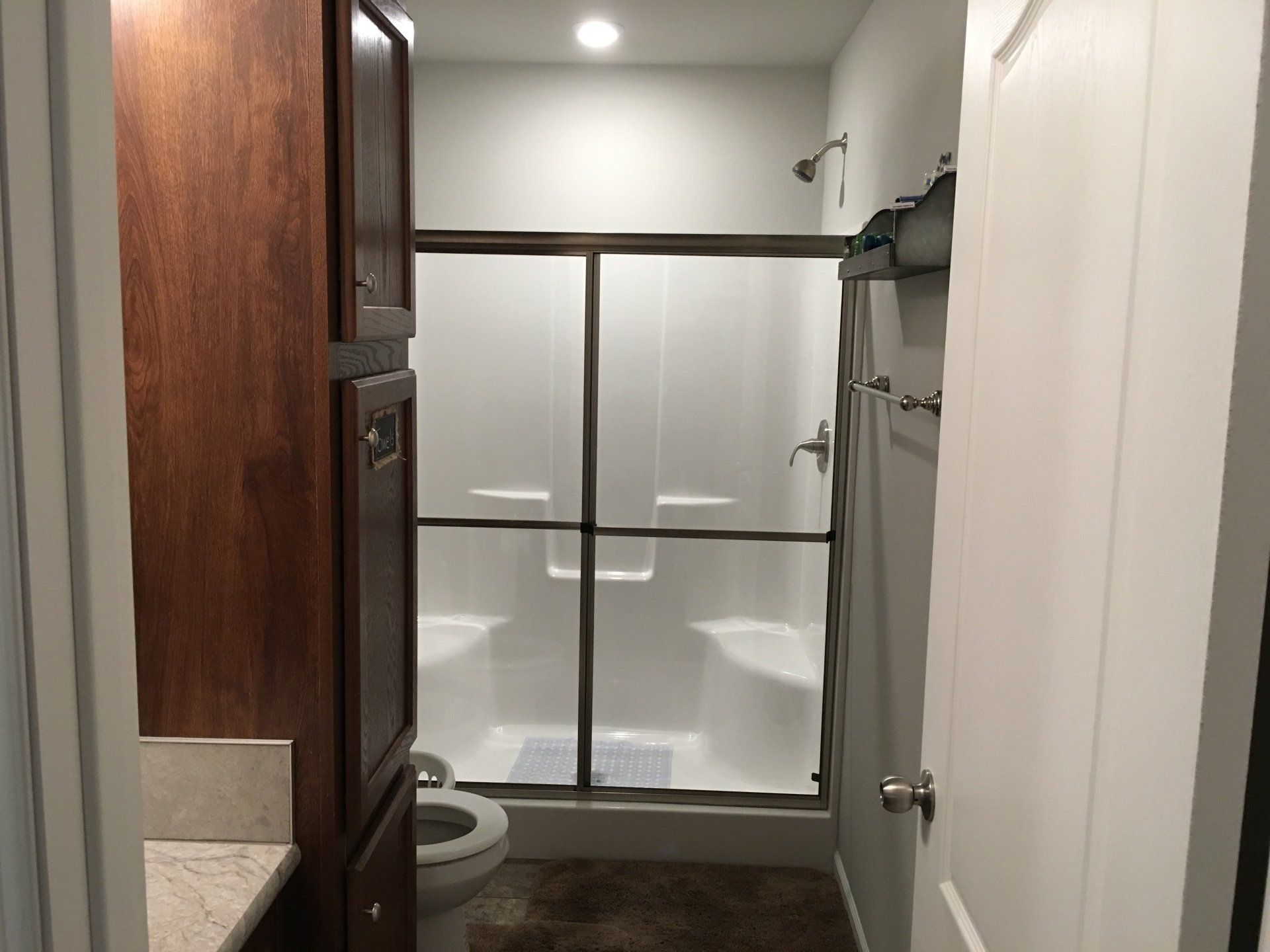 Bathroom with dark wood cabinets, white shower, toilet, and a partially open door.