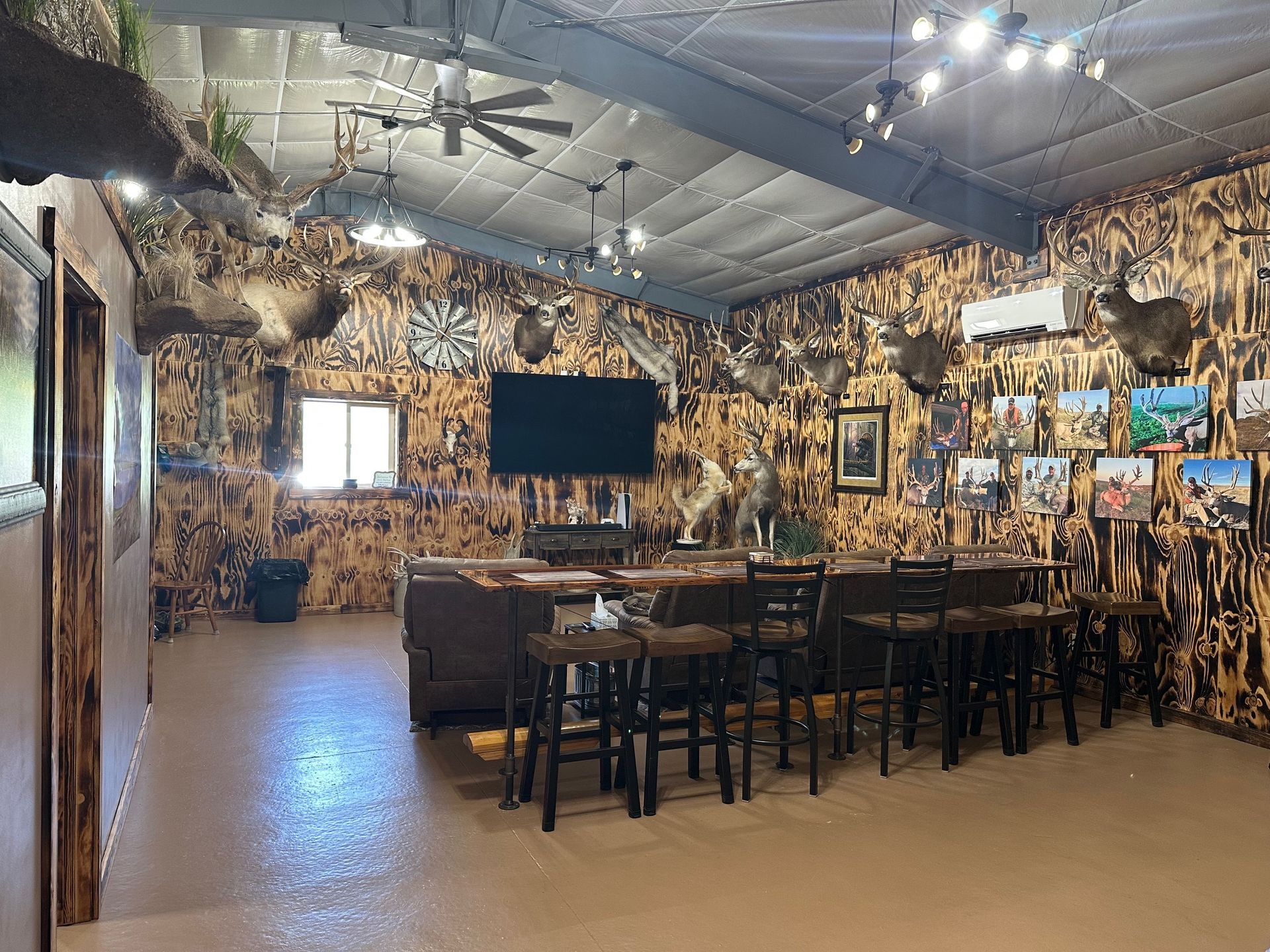 Rustic bar interior with taxidermy, mounted deer heads, a large TV, and bar stools.