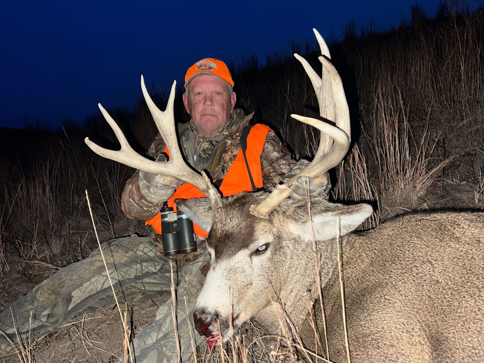 Hunter in orange vest with large buck at dusk.
