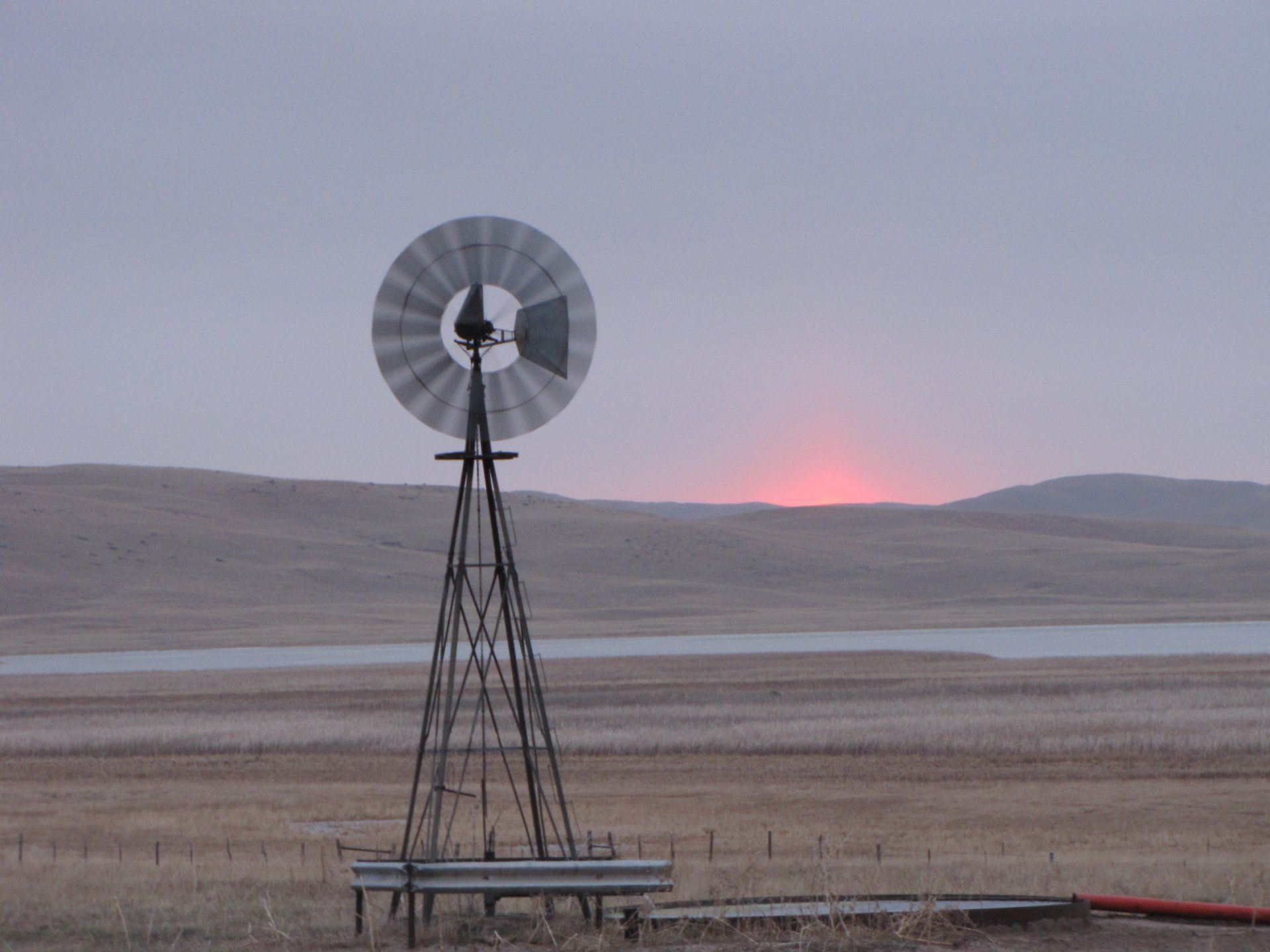 Windmill silhouetted against a dusky sky; landscape with lake and hills.