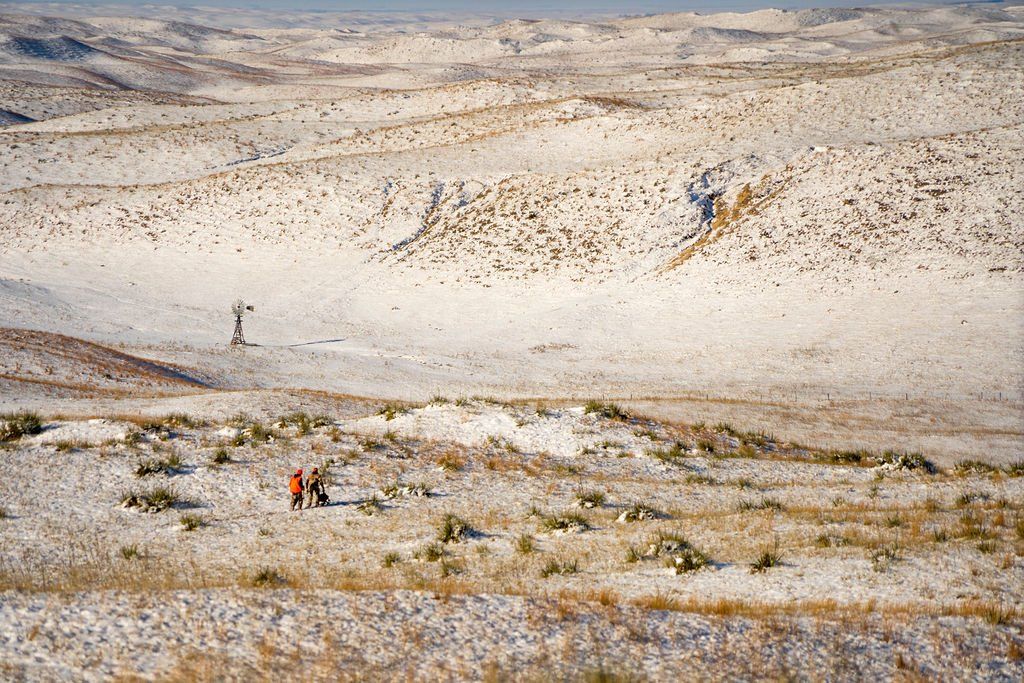 Snow-covered hills with two people, possibly hikers, in orange and brown.
