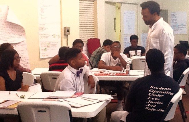 A Group of Students Are Sitting at Desks in a Classroom Talking to a Teacher