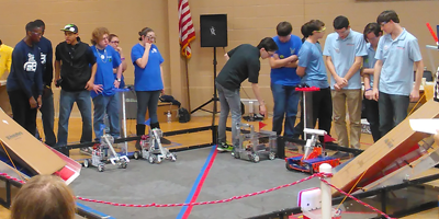 A Group of People Are Standing Around a Robot in a Gym
