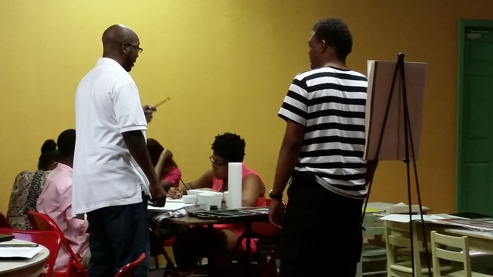 A Man in a Striped Shirt Stands in Front of a Group of People Sitting at Tables