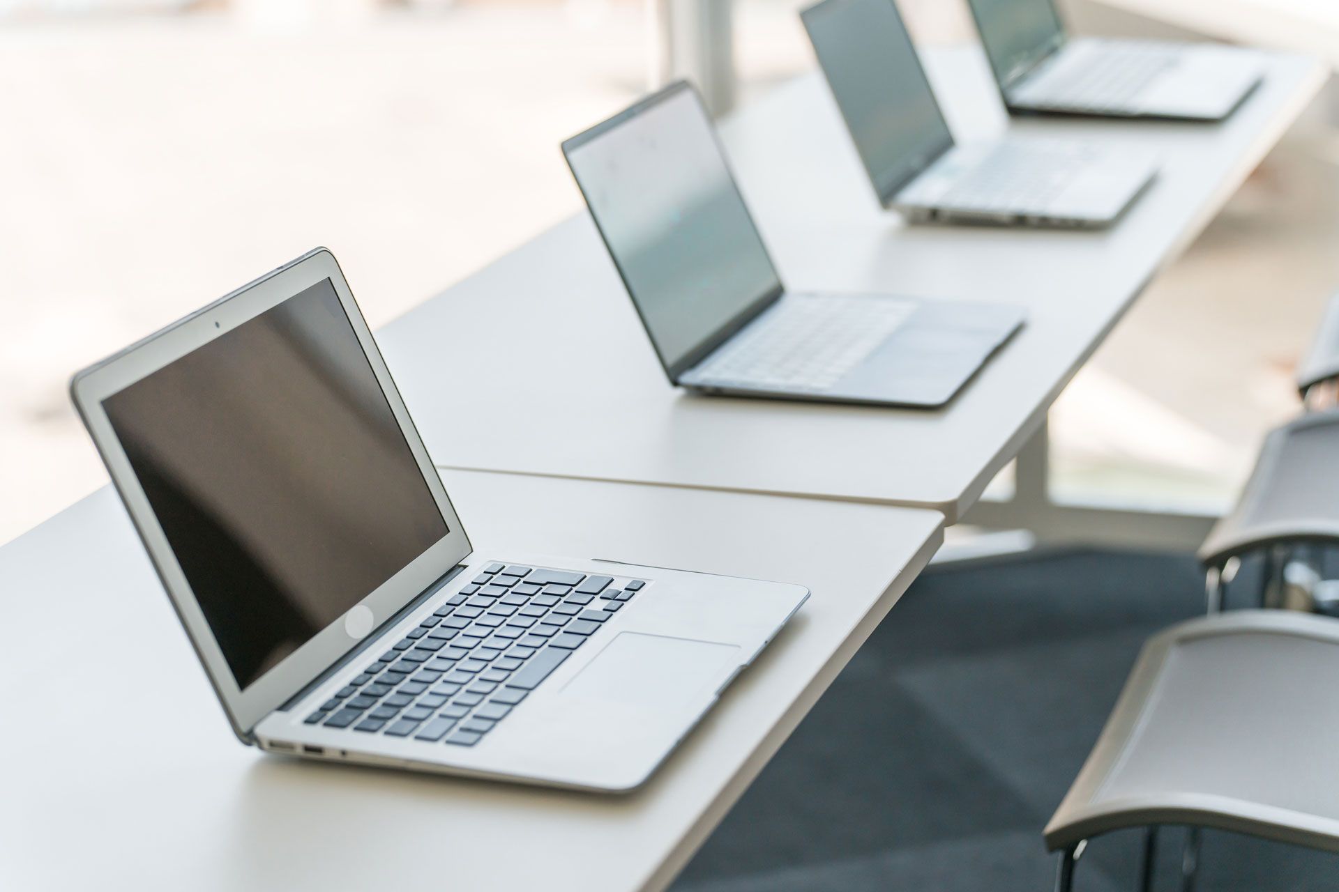 Laptops on a white desk in a room. Three laptops are open, the closest one angled toward the viewer.
