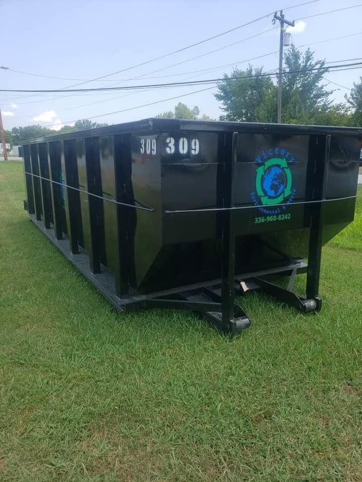 A large black dumpster is sitting on top of a lush green field.
