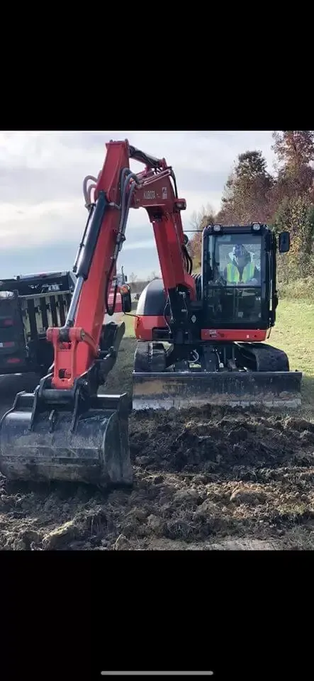 A red excavator is moving dirt in a field.