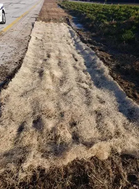 A car is driving down a road next to a pile of dirt.