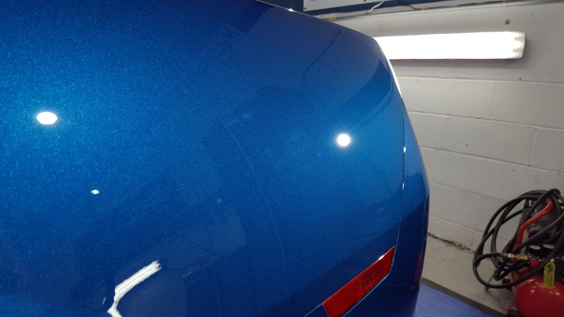 Blue car hood with a red reflector, under a fluorescent light.