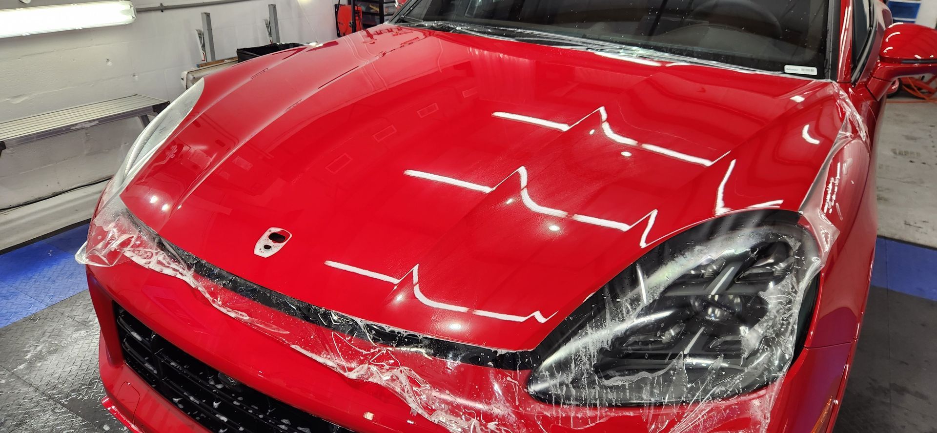 Red car hood with protective film being applied.