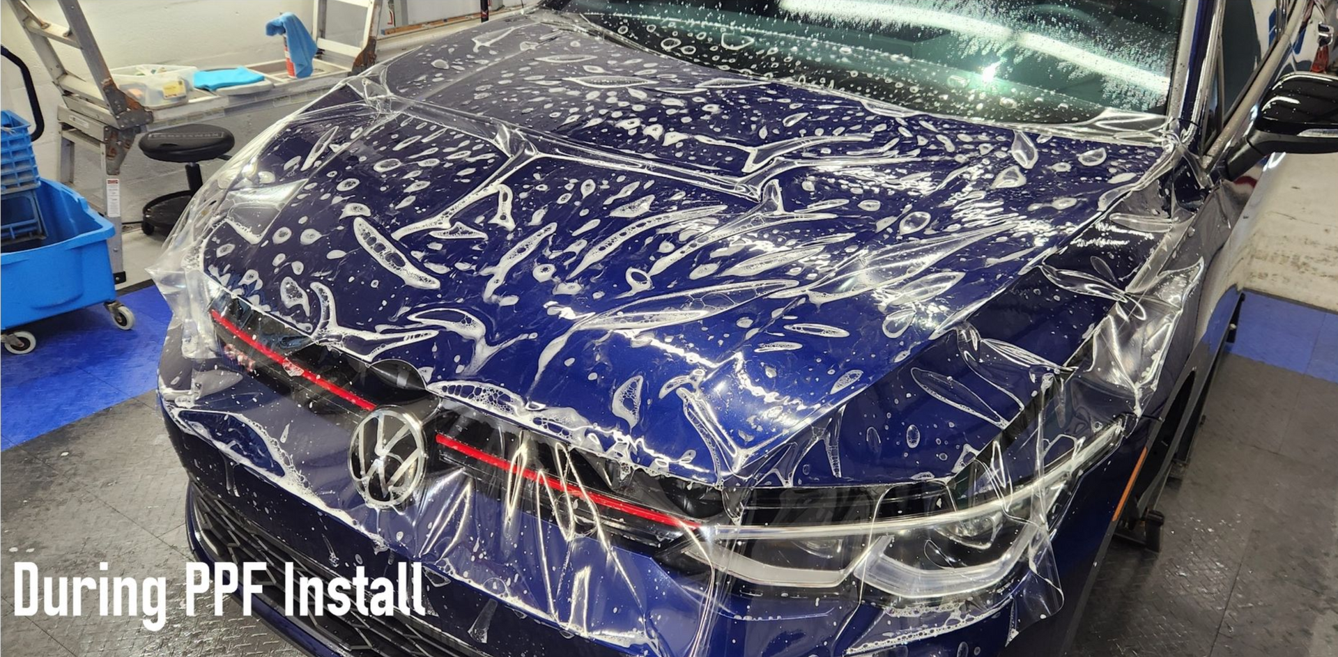 Blue car with clear protective film being applied during a PPF install.