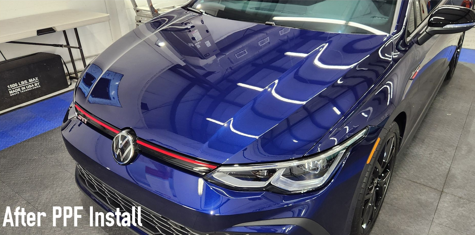 A close-up of a blue Volkswagen car hood with a PPF install, in a garage setting.