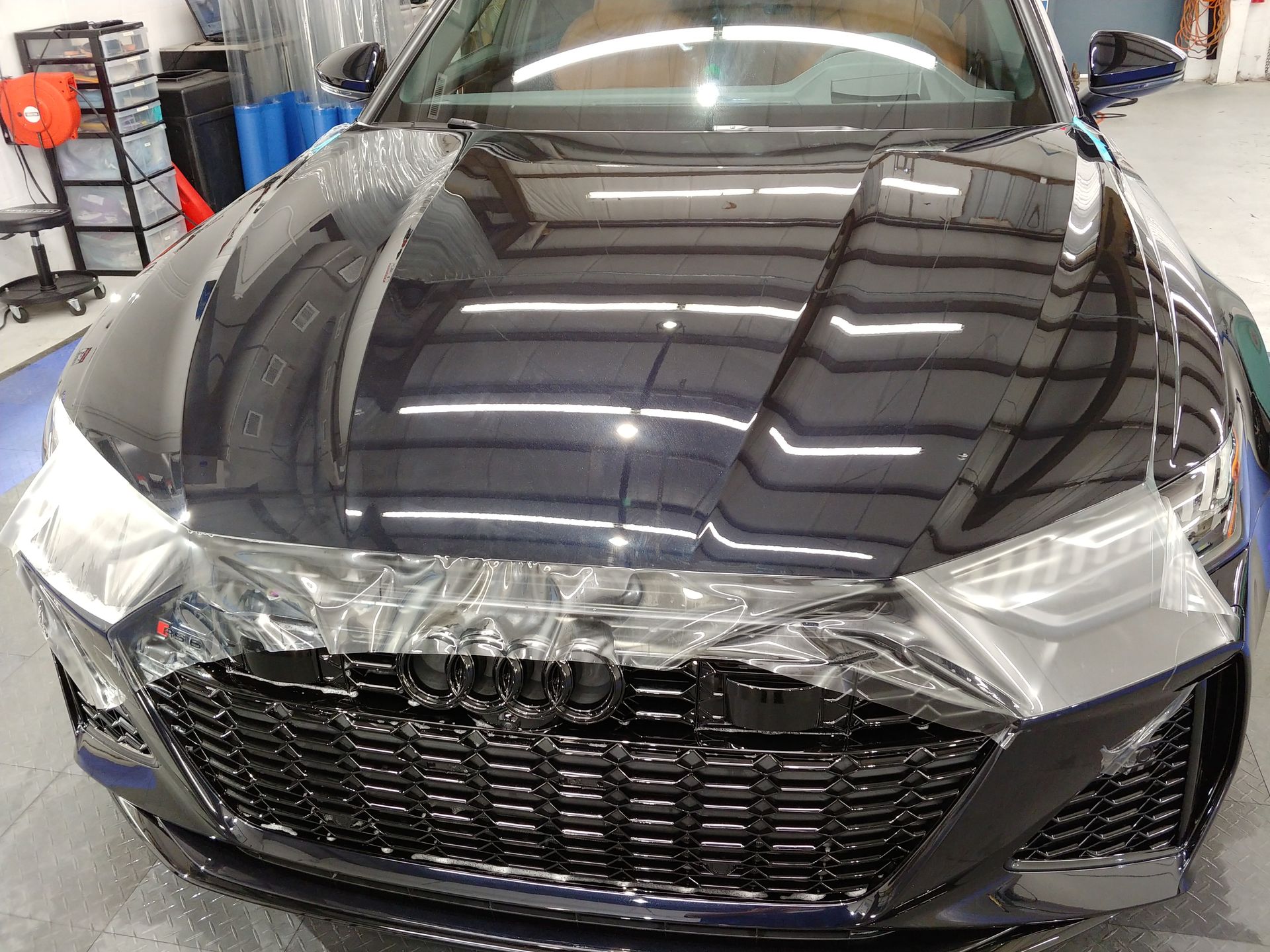 Car hood with protective film applied over the front grill and headlights in a garage setting.