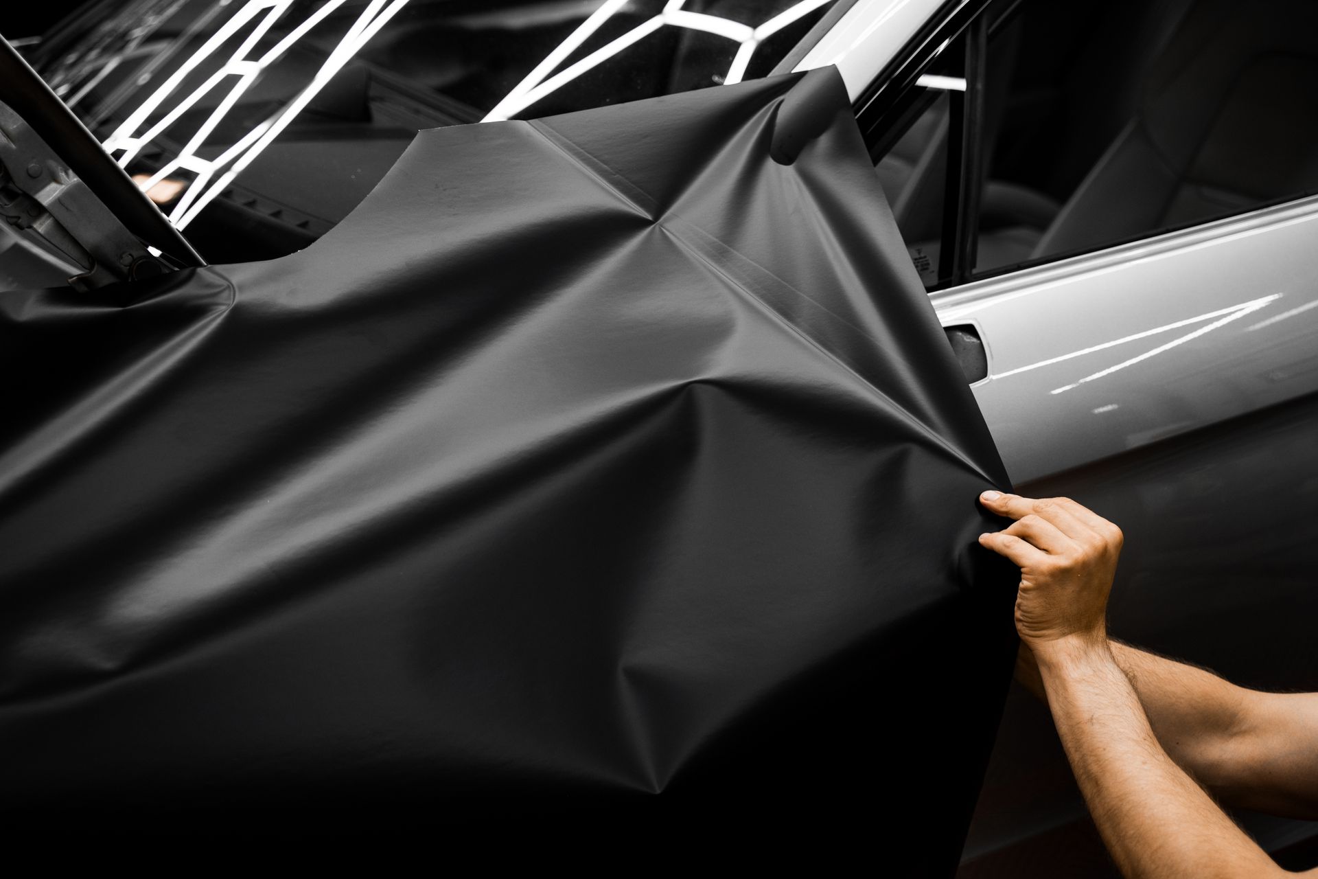Person applying black car wrap to a silver car door.