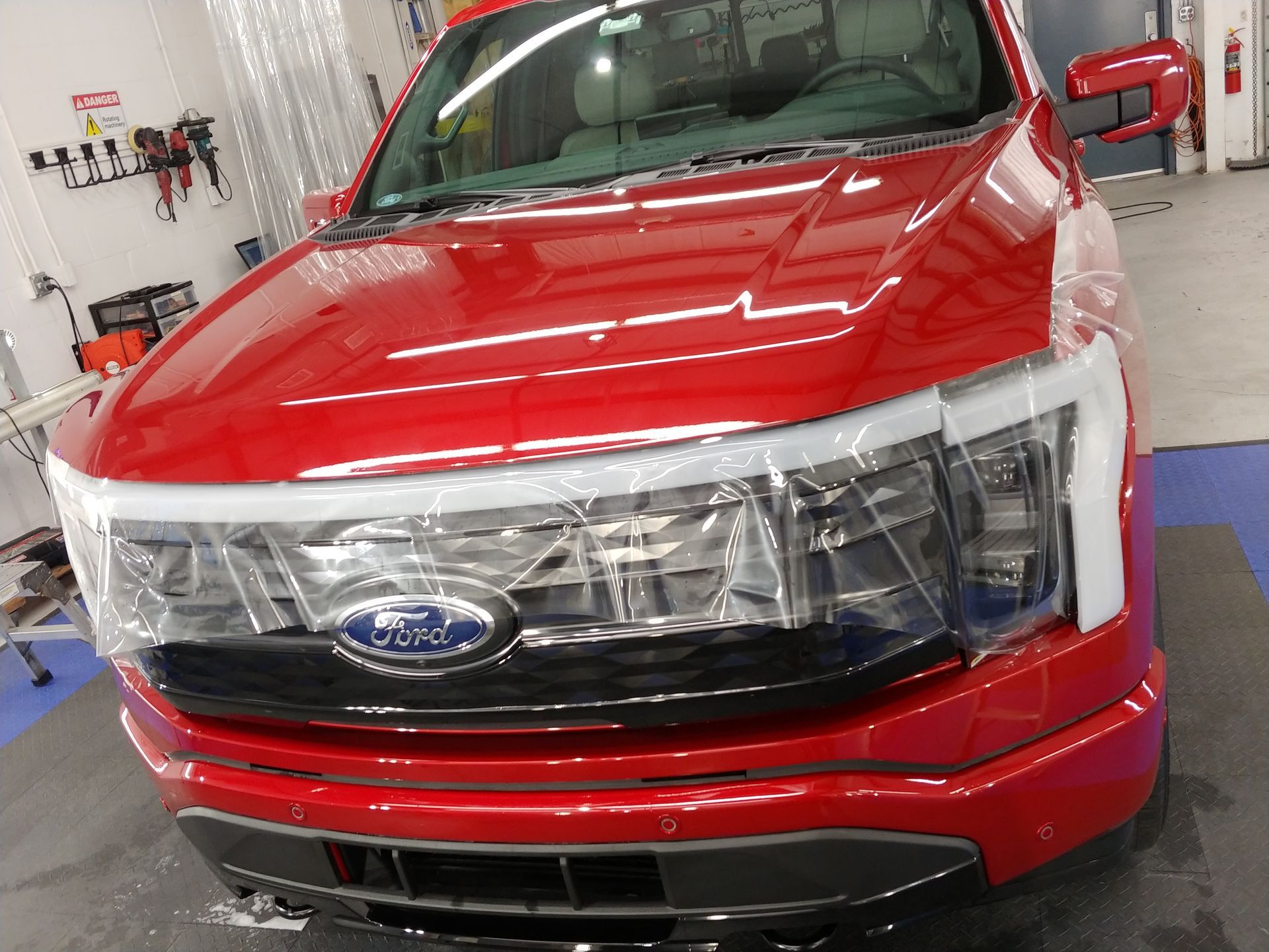 Red Ford pickup truck with protective film on the front in a repair shop.