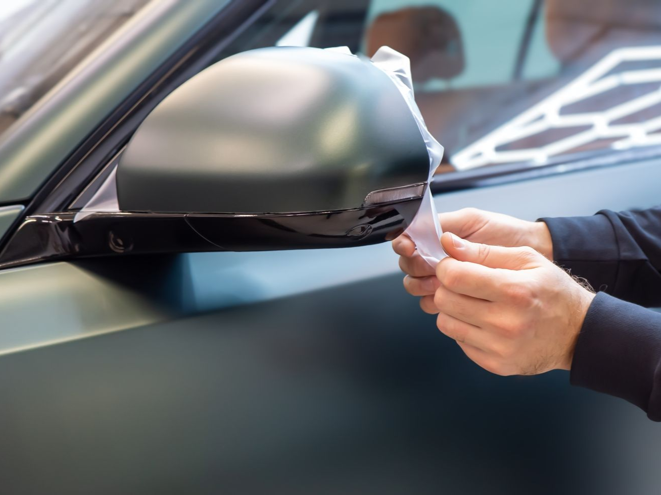 Person applying a film to a matte green car mirror.