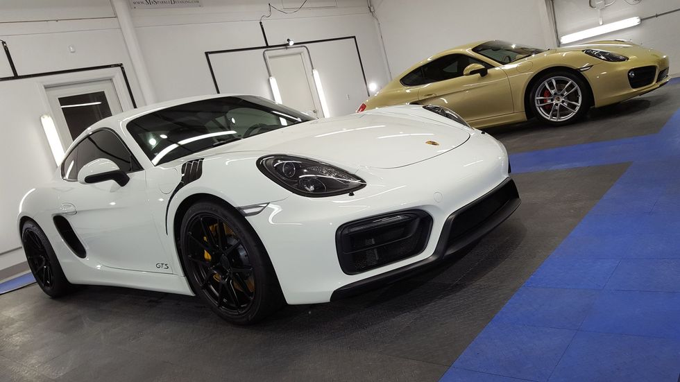 Two Porsche sports cars, one white and one tan, parked indoors on blue flooring.