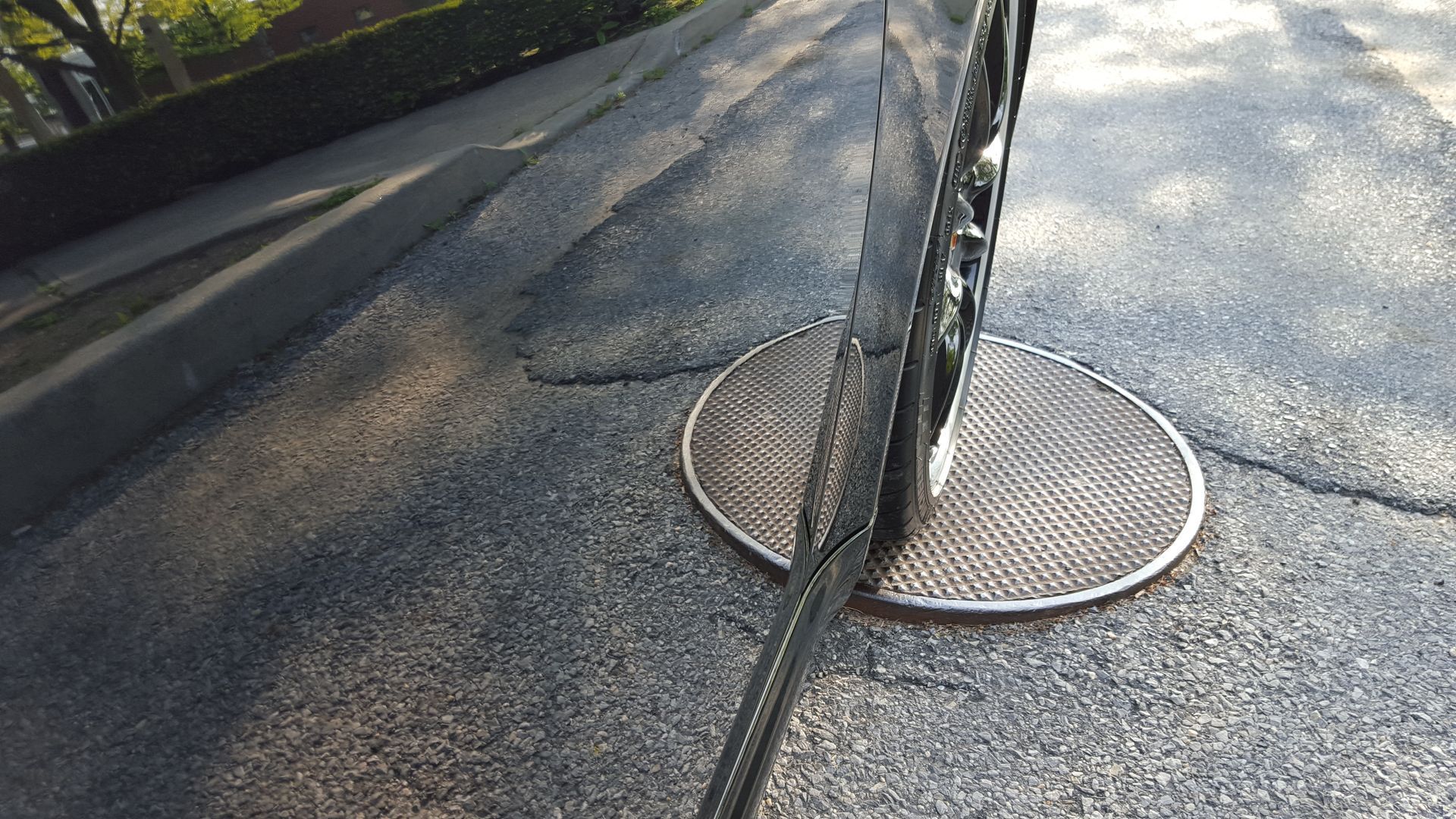 Black car tire parked next to a metal sewer grate in the asphalt.