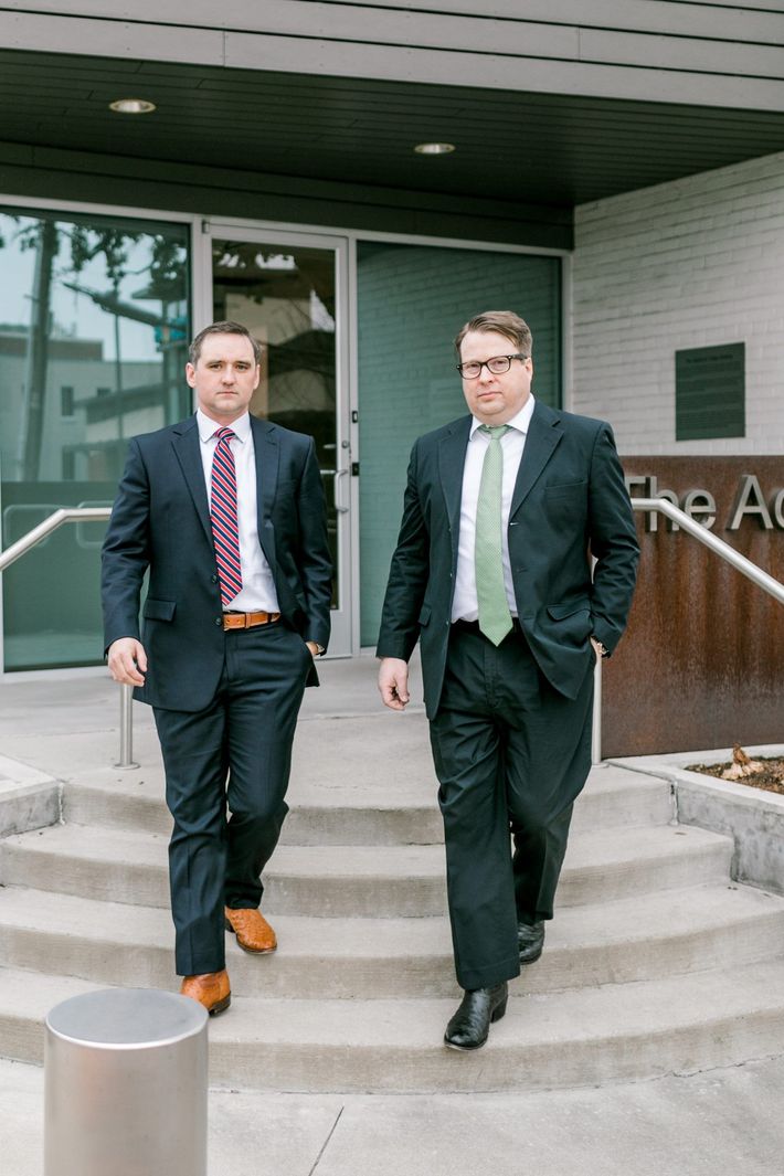 Two men in suits exiting a building, one with a pink tie, the other with a green tie.