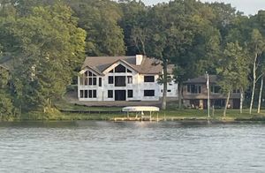 A large house sits on the shore of a lake surrounded by trees.