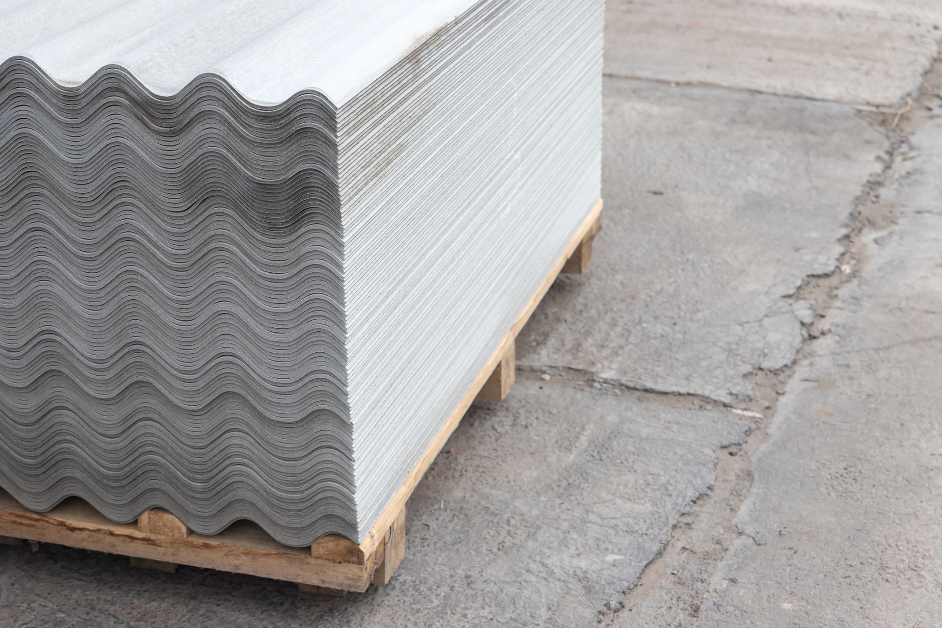 Pila de tejas onduladas de color gris sobre un palé de madera, sobre una superficie de hormigón.
