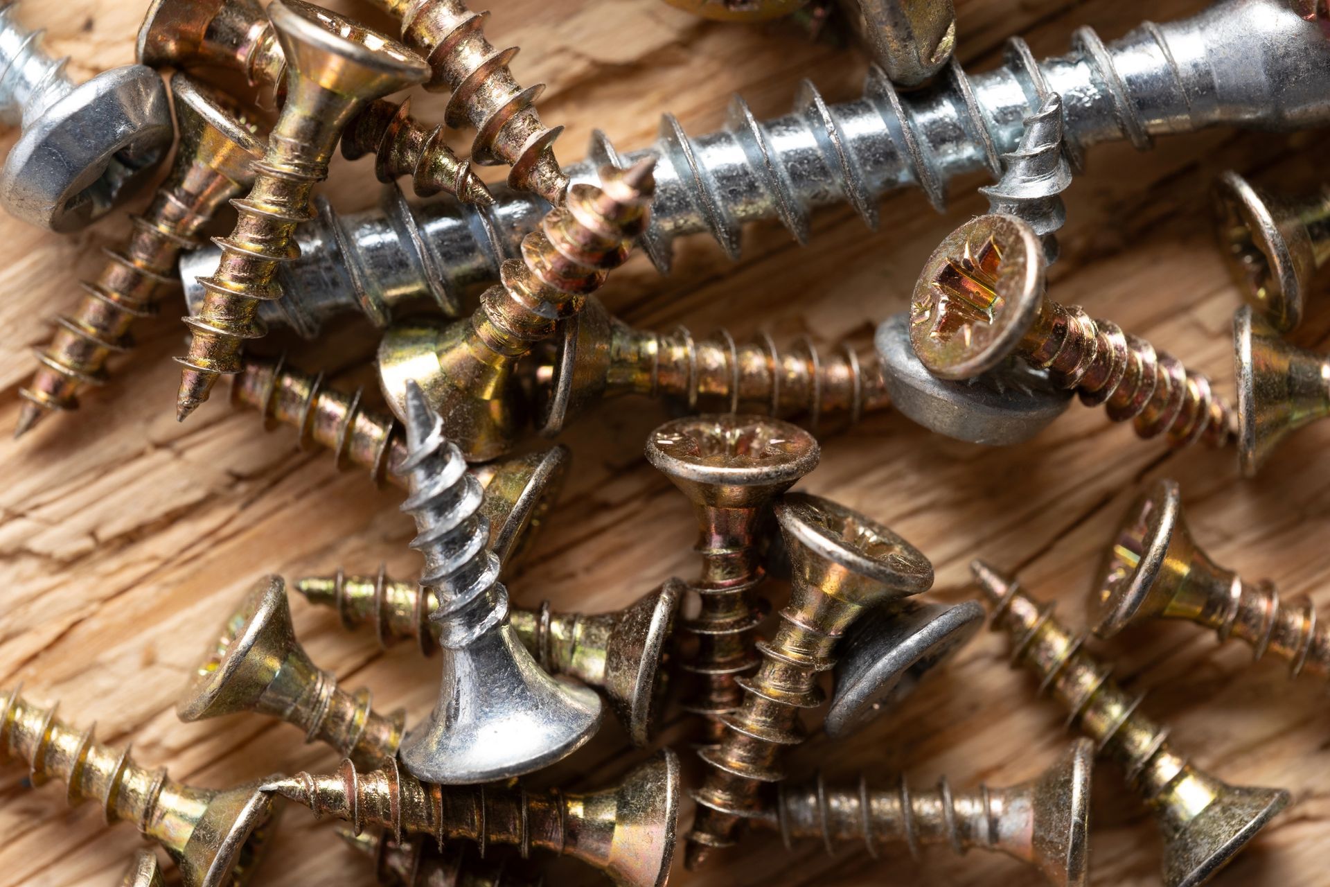 Pila de tornillos surtidos sobre una superficie de madera, de varios colores: plata, oro y marrón.