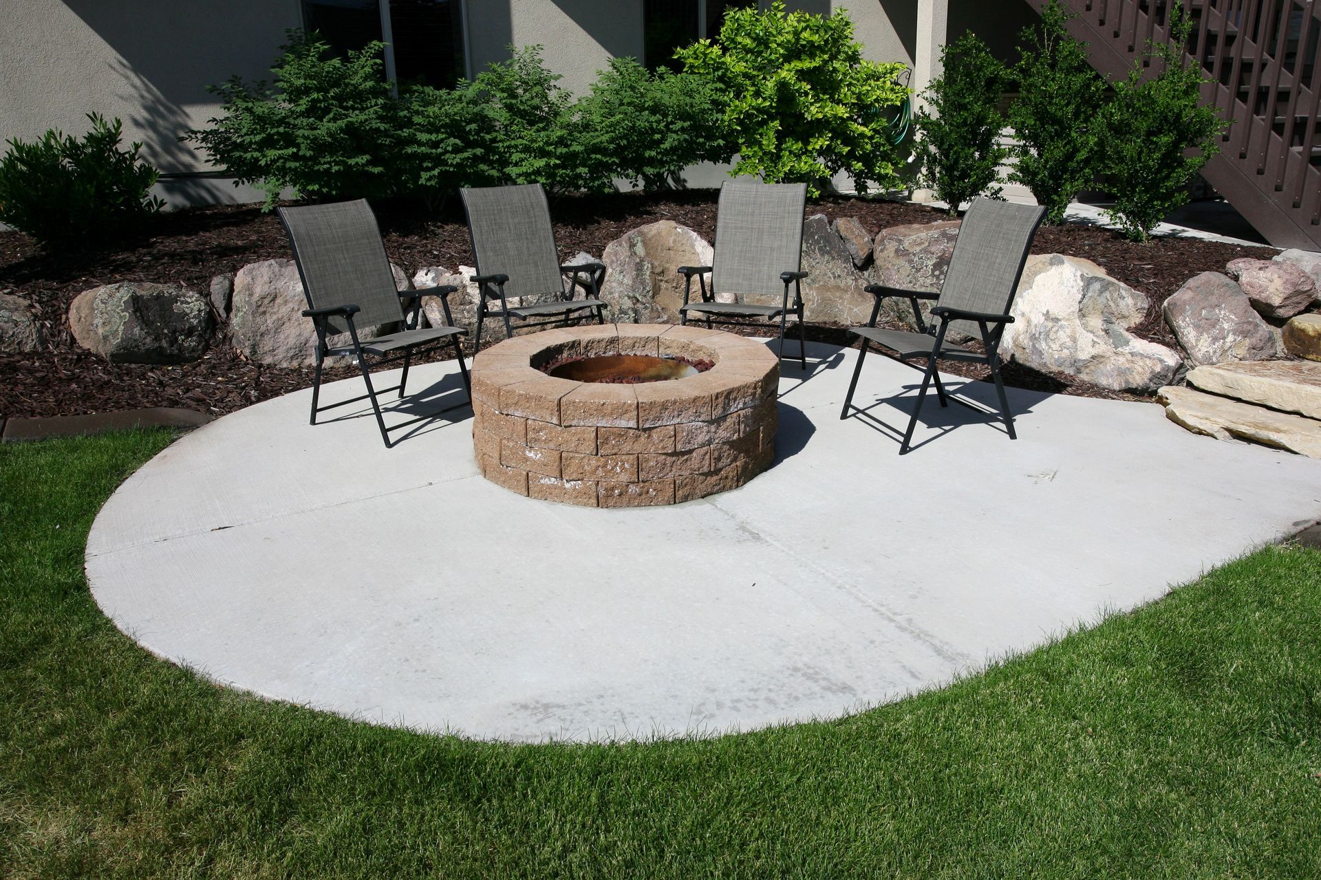 A fire pit in the middle of a patio with chairs around it
