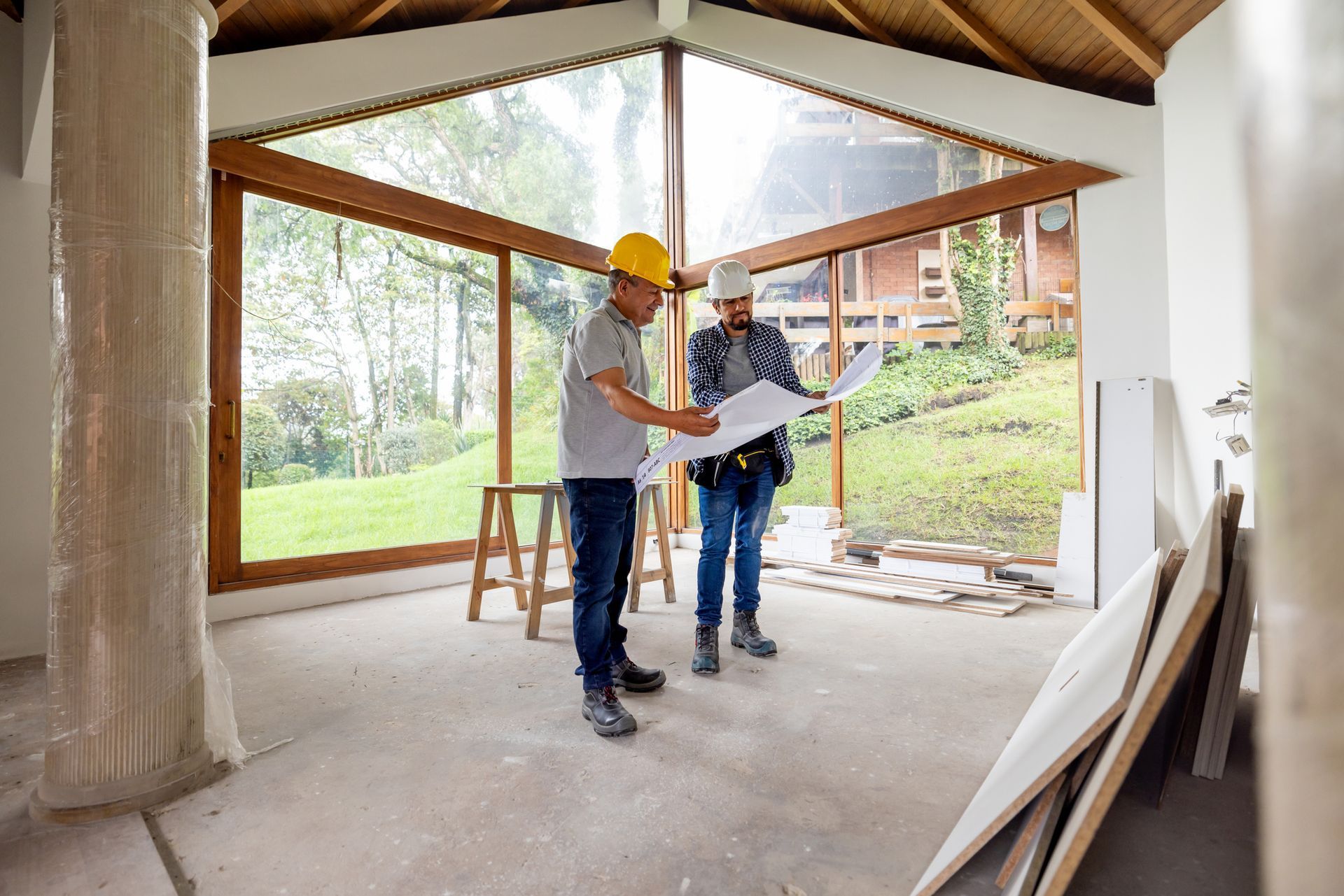 Two construction workers are looking at a blueprint in a room under construction.
