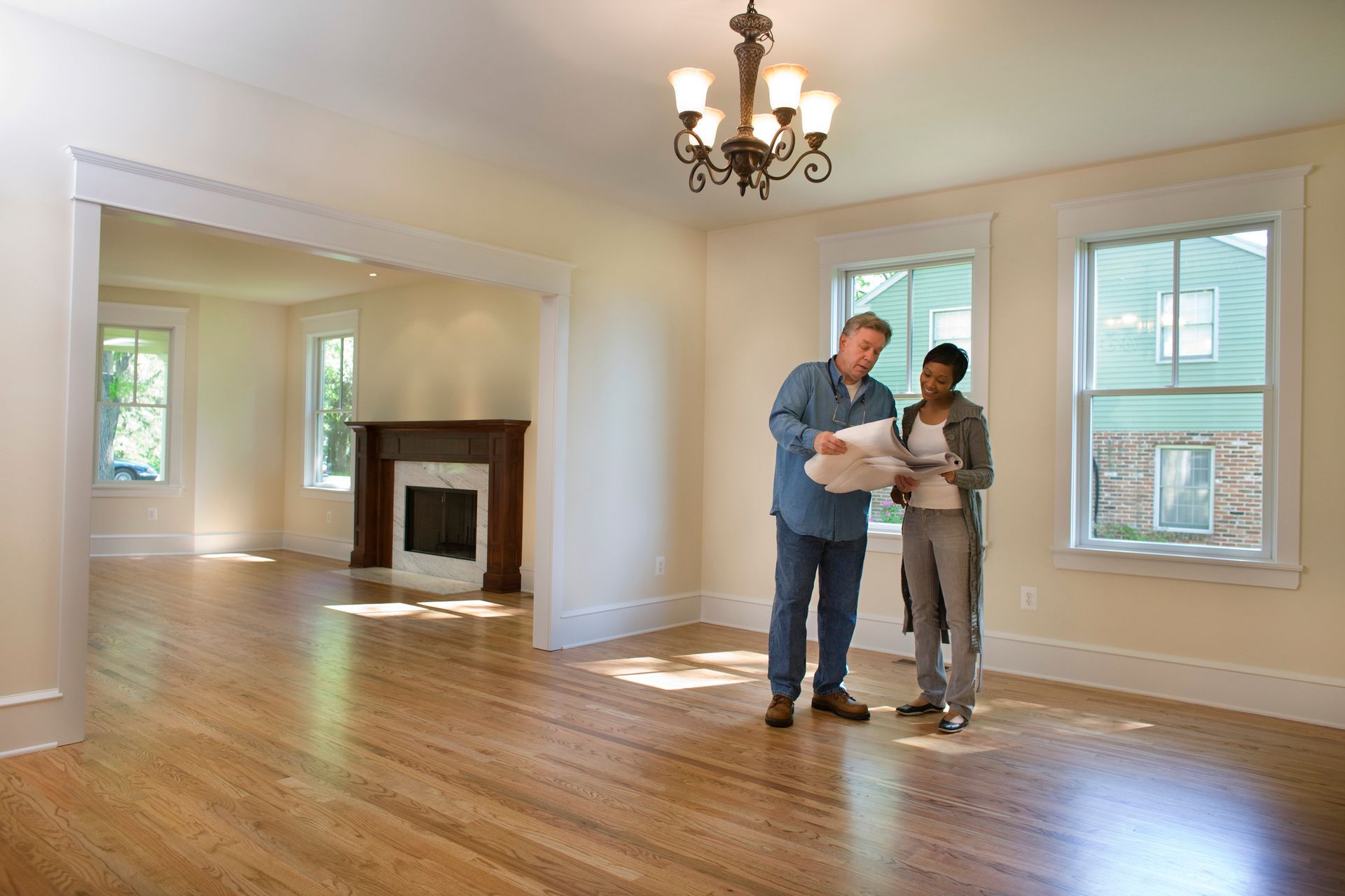 A man and a woman are looking at blueprints in an empty living room.