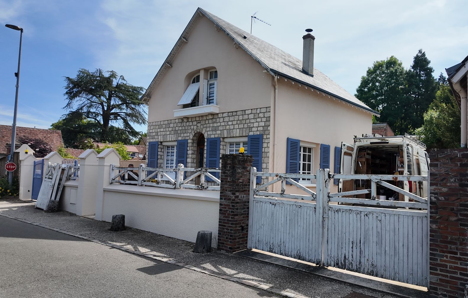 Une maison blanche avec des volets bleus et un portail blanc