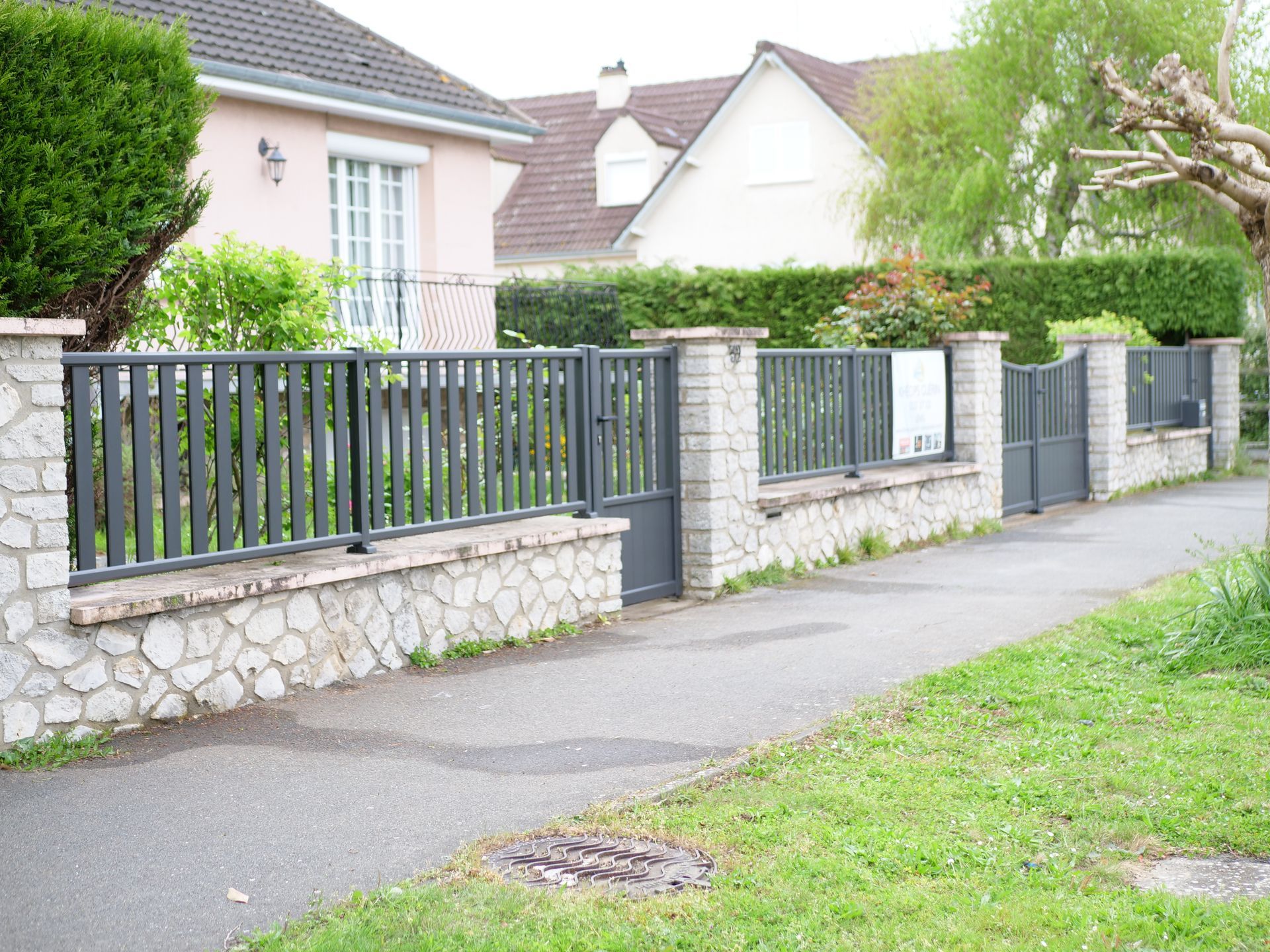 Un mur de pierre avec une clôture et un portail devant une maison
