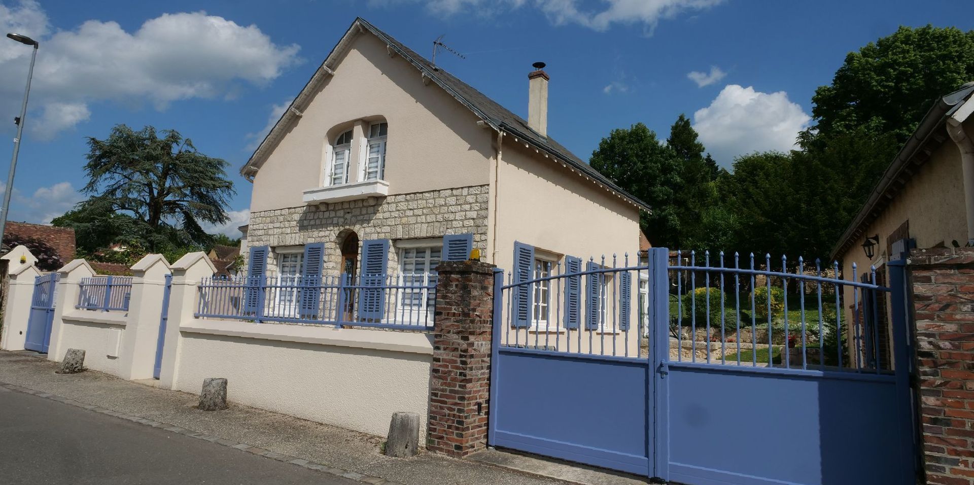 Une maison blanche avec des volets bleus et un portail bleu