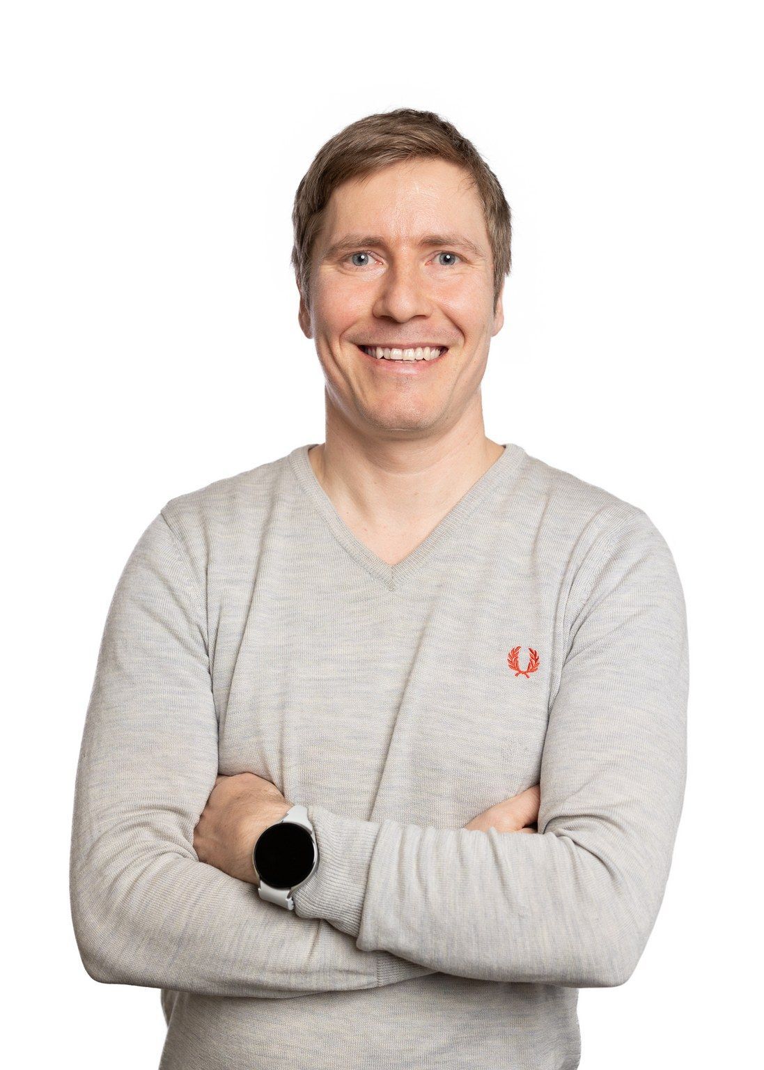 A man in a grey sweater is smiling with his arms crossed.