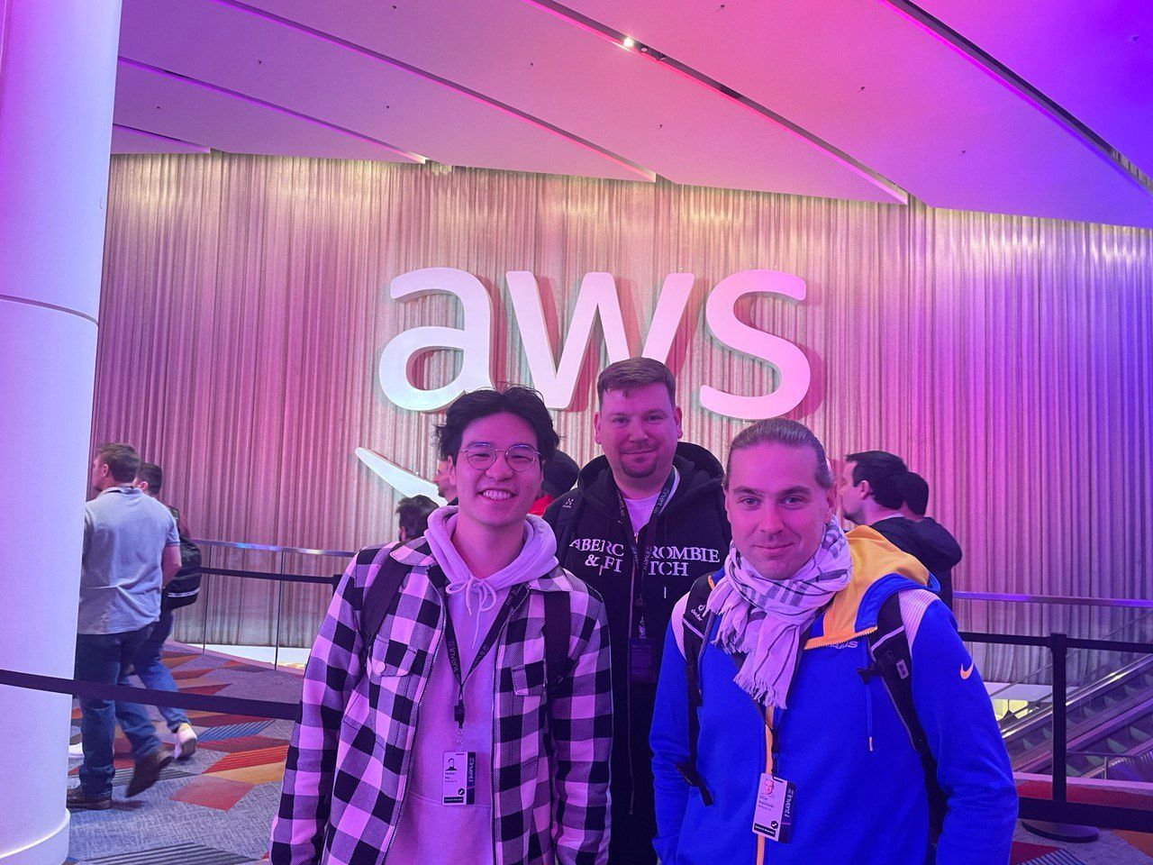 Three men are posing for a picture in front of a aws sign.