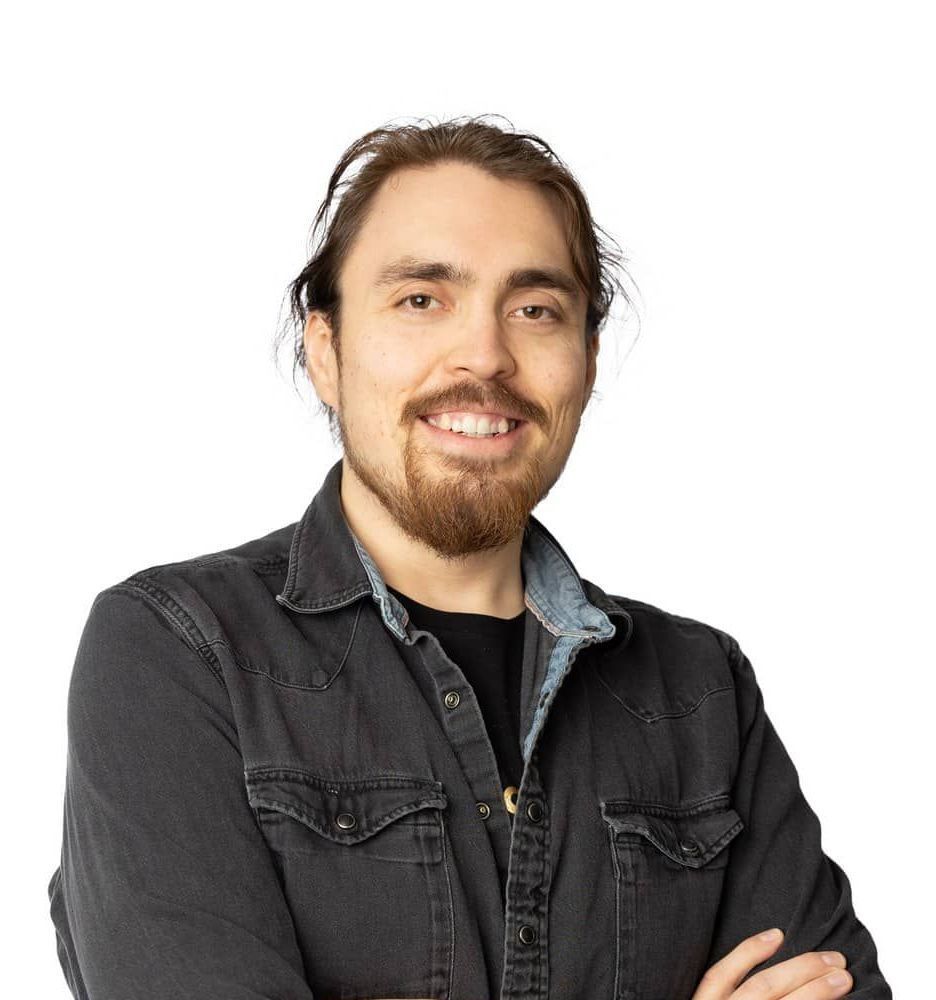 A man with a beard is wearing a black shirt and a denim jacket.