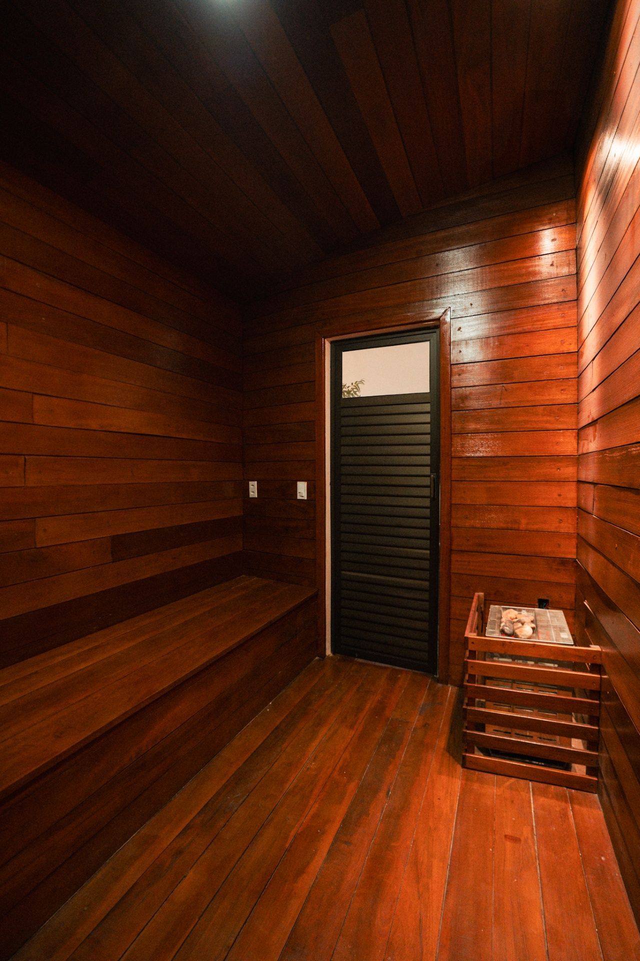 Uma sauna de madeira com um banco embutido, uma porta e um aquecedor no chão.
