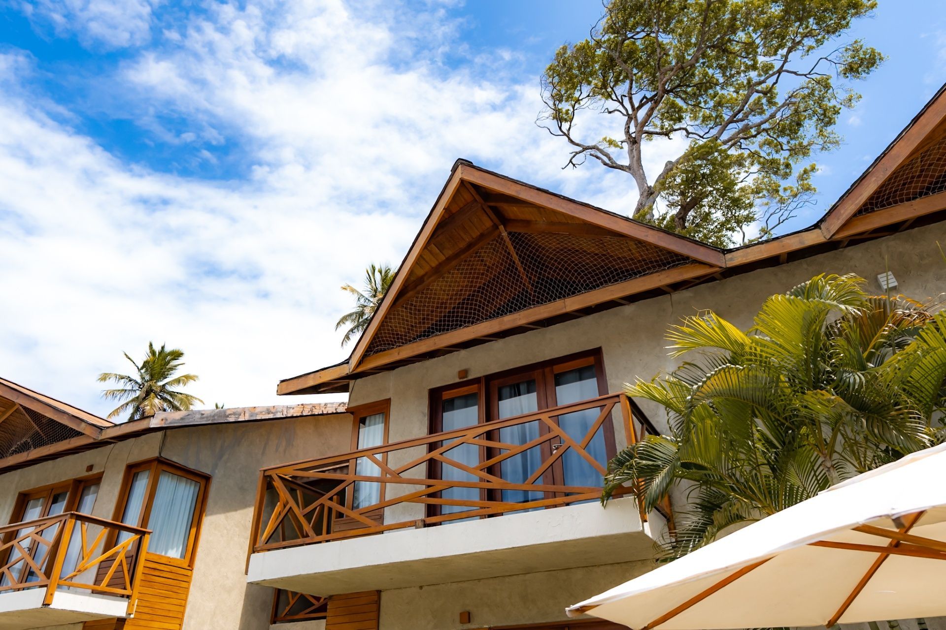 Prédio de dois andares em um resort tropical com varandas de madeira e telhados de duas águas sob um céu azul parcialmente nublado.
